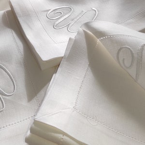May include: Three white linen napkins with a white embroidered letter "W" on each. The napkins are folded and stacked on top of each other.