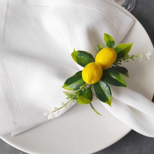 May include: White linen napkin with a lemon napkin ring. The ring is made of burlap and has two small yellow lemons with green leaves.
