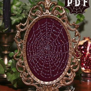May include: An oval frame in a gold colour, featuring a burgundy backdrop with a beaded spiderweb design. The frame has an elaborate, vintage design. The text "PDF" is in the upper right corner. The frame is supported by a decorative stand.