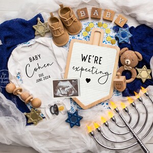 Może przedstawiać: Ogłoszenie o ciąży z białym body z napisem "Baby Cohen Due June 2024". Ogłoszenie zawiera buciki dziecięce, znak z napisem "We're expecting", USG i menorę.