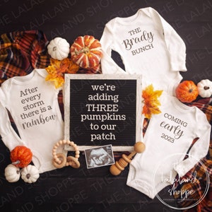 以下が含まれることがあります： 3つのロンパースと文字盤を使った妊娠発表。ロンパースは白地に茶色の文字で、「嵐の後は必ず虹が架かる」「ザ・ブレイディ・バンチ」「2023年初めにやってくる」と書かれている。文字盤には「私たちはパッチに3つのカボチャを追加します」と書かれている。