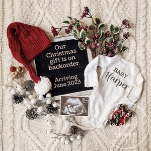 Könnte beinhalten: Ein weißer Strampler mit dem Text "BABY Harper" darauf, eine rote Weihnachtsmütze mit einem weißen Bommel, eine schwarze Buchstabenwand mit dem Text "Our Christmas gift is on backorder Arriving June 2023", ein Schwarzweiß-Ultraschallbild und eine kleine rote Glocke mit dem Text "the lalaland shoppe" darauf.