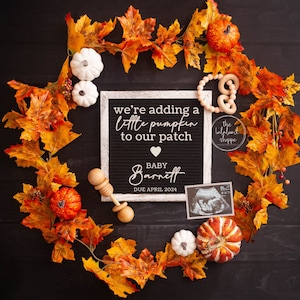 Peut inclure: Annonce de grossesse sur fond noir. Une couronne de feuilles d'automne entoure un tableau de lettres en feutre avec le texte "we're adding a little pumpkin to our patch" et "Baby Barnett Due April 2024". Des citrouilles décoratives et un hochet sont également inclus.