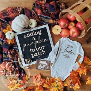 May include: A white onesie with the text "Baby Jordan Due October 2022" on it. A black letter board with the text "Adding a pumpkin to our patch" is in the background. There are pumpkins, apples, and fall leaves around the onesie.