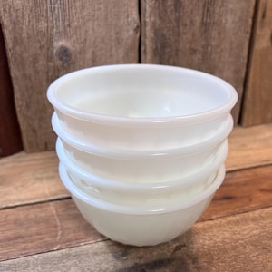May include: A stack of four white, round bowls. The bowls have a simple, classic design with a slightly flared rim and a ridged texture around the sides. The bowls are made of a milky white material.