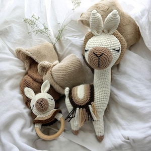 Könnte beinhalten: Eine Sammlung handgefertigter Baby-Spielzeuge aus Häkelarbeit. Enthalten sind ein weißes Lama mit braunen Akzenten, eine passende Rassel und ein Paar Babyschuhe. Die Spielzeuge sind in neutralen Tönen gehalten, ideal für ein Babyzimmer.