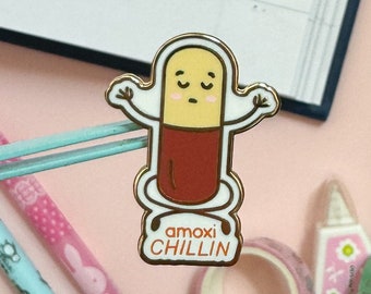以下が含まれることがあります： 顔と「amoxichilling」という文字が書かれた漫画の錠剤が描かれた金色のエナメルピンです。