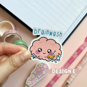 May include: A pink brain-shaped sticker with a cute face and a sponge in its hand, surrounded by soap bubbles. The sticker says "brainwash" in blue text.