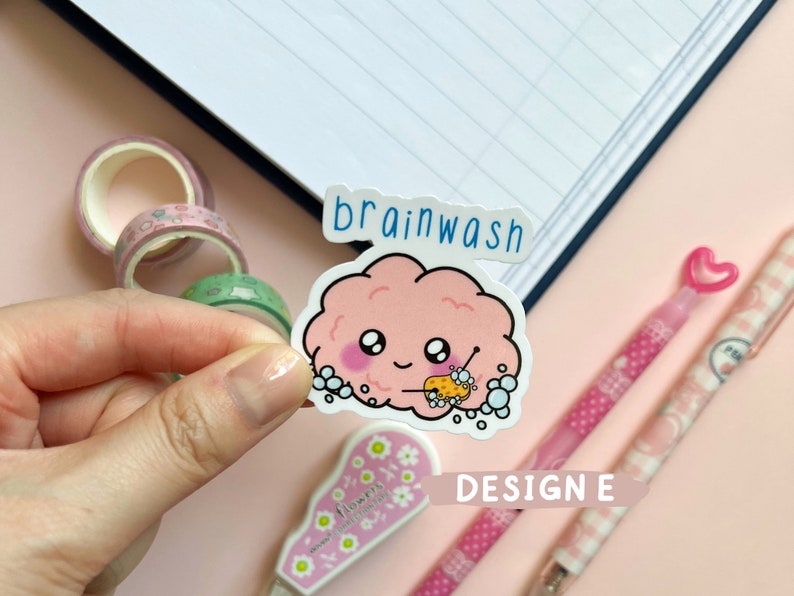 May include: A pink brain-shaped sticker with a cute face and a sponge in its hand, surrounded by soap bubbles. The sticker says "brainwash" in blue text.