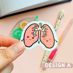 May include: A sticker of two pink cartoon lungs with smiling faces and black outlines. The lungs are holding hands and have a white bronchial tube connecting them. The sticker is on a pink background.