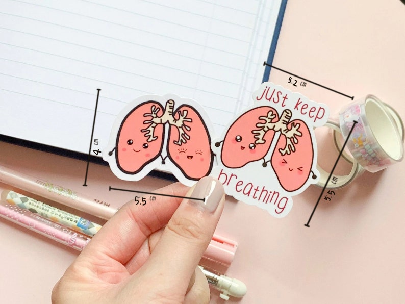May include: Two pink cartoon lungs with smiling faces and the text "just keep breathing" on a white background. The sticker is 5.5 cm wide and 5.2 cm tall.