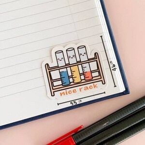 Peut inclure: Un autocollant blanc avec une illustration de quatre tubes &agrave; essai dans un support. Les tubes &agrave; essai ont des visages heureux et sont remplis de liquides bleus, jaunes et oranges. Le texte "nice rack" est &eacute;crit sous le support. L'autocollant mesure 5,5 cm sur 4,0 cm.