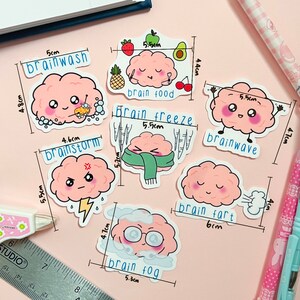 May include: Eight pink brain-shaped stickers with different expressions and text. The stickers are labeled with different brain-related terms, such as "brainwash", "brainstorm", "brain food", "brain freeze", "brainwave", "brain fart", and "brain fog".