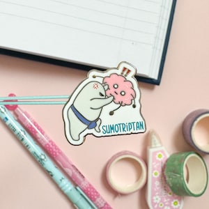 May include: A white enamel pin with a cartoon illustration of a white creature with a blue bow tie and a pink brain with a surprised expression. The text "SUMOTRIPTAN" is below the illustration.