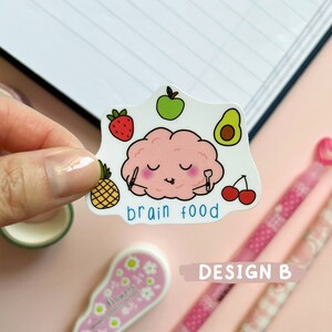 May include: A sticker with a pink brain eating a pineapple, avocado, strawberry, and cherries. The sticker says "brain food".
