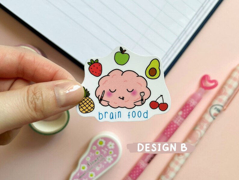 May include: A sticker with a pink brain eating a pineapple, avocado, strawberry, and cherries. The sticker says "brain food".