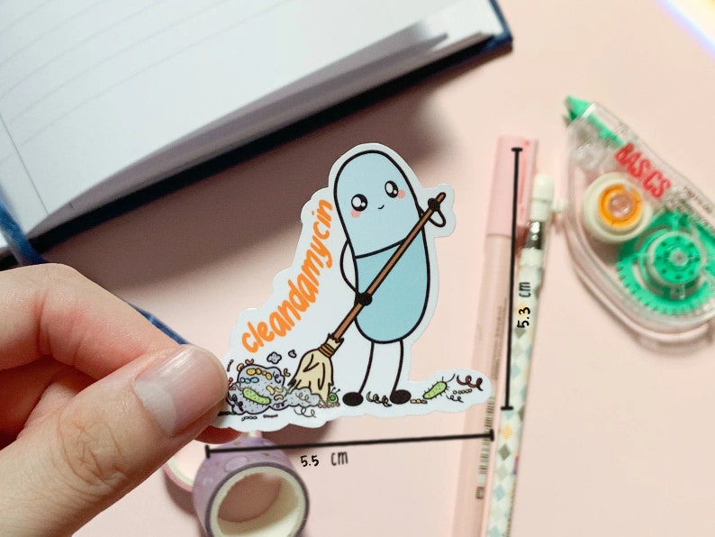 Puede incluir: Un personaje azul con forma de p&iacute;ldora con una cara amigable sostiene una escoba y barre un mont&oacute;n de bichos coloridos. El texto "cleandamycin" est&aacute; escrito en la escoba. La pegatina mide 5,5 cm de ancho.