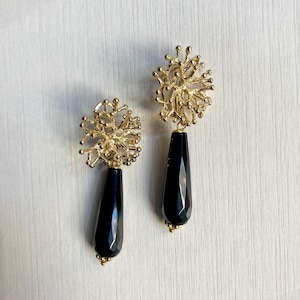 Può includere: Un paio di orecchini dorati con pietre nere a forma di goccia. Gli orecchini presentano un design delicato e intricato che ricorda il corallo.