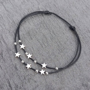 May include: A black string bracelet with silver star charms. The bracelet is double-layered and has a simple knot closure.