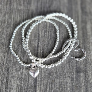 May include: Three silver beaded bracelets with a heart charm and a larger open heart charm.