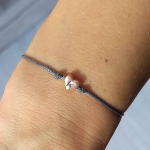 May include: A grey string bracelet with a small rose gold heart charm.