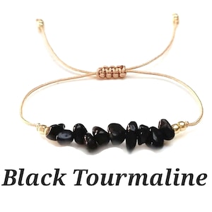 May include: A black tourmaline gemstone bracelet with a beige cord and gold beads. The bracelet is adjustable with a sliding knot.