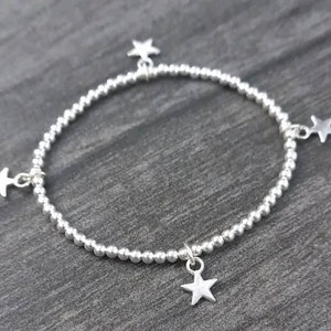 May include: A silver beaded bracelet with four silver star charms hanging from it.