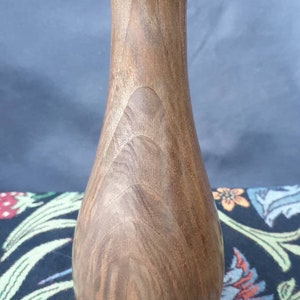 May include: A dark brown wooden vase with a smooth, rounded shape. The vase has a narrow neck and a wide base.