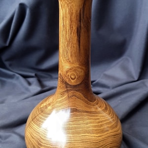 May include: A wooden vase with a wide base and a narrow neck. The vase is made of dark wood with a natural grain pattern. The vase is polished and has a glossy finish.