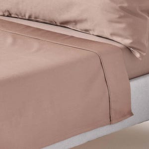 May include: A close-up of a light brown fitted sheet with a smooth, wrinkle-free finish. The sheet is tucked into a light grey mattress.