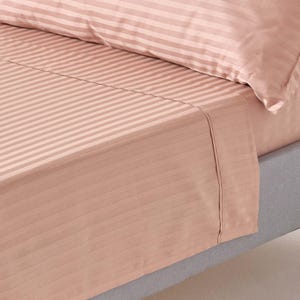 May include: A close-up of a pink striped fitted sheet with a subtle sheen. The sheet is tucked into a grey mattress.