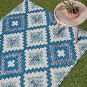 May include: A blue and white outdoor rug with a geometric pattern. The rug features a repeating design of squares and crosses in shades of blue and white. The rug is made of a durable material and is suitable for outdoor use.