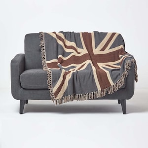 May include: A grey armchair with a Union Jack flag throw blanket draped over it. The blanket is in shades of brown, beige, and grey, with a fringed edge. The armchair has black legs and is set against a white background.