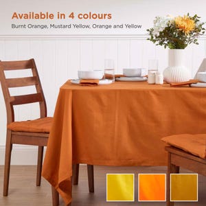 May include: A burnt orange tablecloth on a wooden table, set for a meal with white dishes, napkins, and glasses. The text "Available in 4 colours" is at the top, with colour swatches of yellow, orange, and burnt orange.