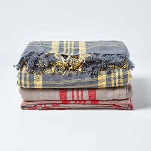 May include: A stack of three woven blankets. The top blanket is gray and yellow plaid with fringe. The middle blanket is beige with red stripes. The bottom blanket is beige.