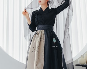 May include: A black and beige hanbok with a floral print. The hanbok has a long skirt and a fitted top with a high collar. The woman is wearing a black veil over her head.