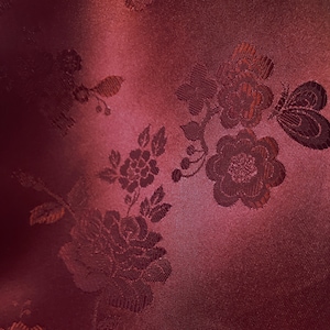 May include: A close-up of a burgundy fabric with an embossed floral pattern. The fabric has a subtle sheen and a soft texture.