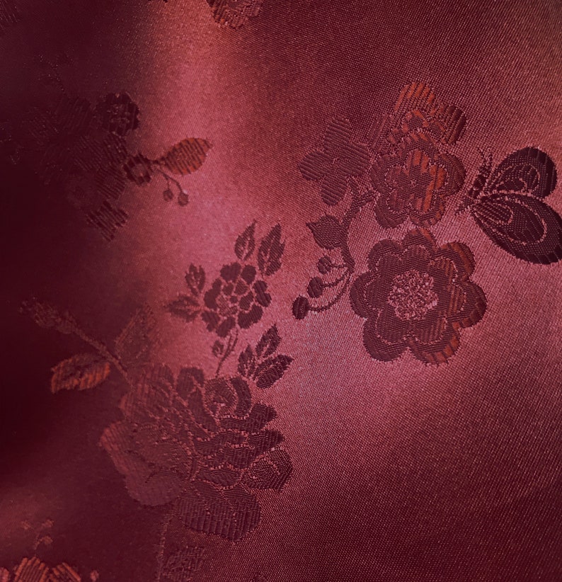 May include: A close-up of a burgundy fabric with an embossed floral pattern. The fabric has a subtle sheen and a soft texture.