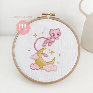 May include: A cross-stitch pattern featuring a pink Pokemon character flying over a yellow crescent moon with pink clouds and white stars on a white background.
