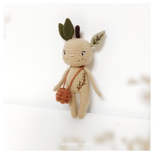Peut inclure: Un jouet en peluche crocheté en forme de personnage humanoïde avec des feuilles sur la tête et un petit sac crocheté marron. Le jouet est beige avec des yeux bruns et un motif de feuilles vertes sur son corps.