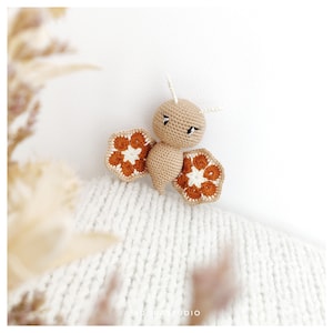 May include: A crocheted bee toy with brown and white wings. The bee has a brown body with white eyes and a small black mouth.