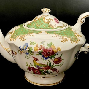Peut inclure: Une théière blanche avec un motif floral vert et or et un motif d'oiseau. La théière a un couvercle avec un bouton en or et une bordure dorée autour du bord.