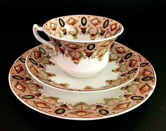 May include: A vintage teacup and saucer set with a delicate floral pattern in shades of brown, green, and white. The set features a geometric design with diamond shapes and a scalloped edge.