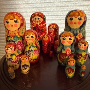 May include: A collection of Russian nesting dolls, or Matryoshka dolls, in various sizes. The dolls are painted with floral designs and feature smiling faces. The color palette includes red, green, yellow, and blue.