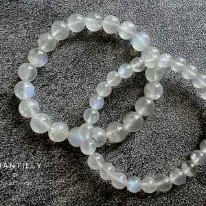 May include: Two white moonstone bracelets with a shimmery iridescent finish. The bracelets are made of round beads and are stacked on top of each other.