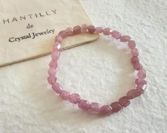 May include: A pink crystal bracelet composed of small, faceted beads. The bracelet is displayed on a white surface next to a small, off-white pouch with the text "CHANTILLY de Crystal Jewelry".
