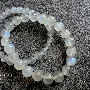 May include: Two white moonstone bracelets with iridescent shimmer. The bracelets are made of round beads and are stacked on top of each other.