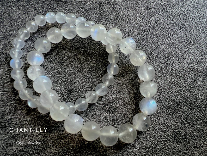 May include: Two white moonstone bracelets with iridescent shimmer. The bracelets are made of round beads and are stacked on top of each other.