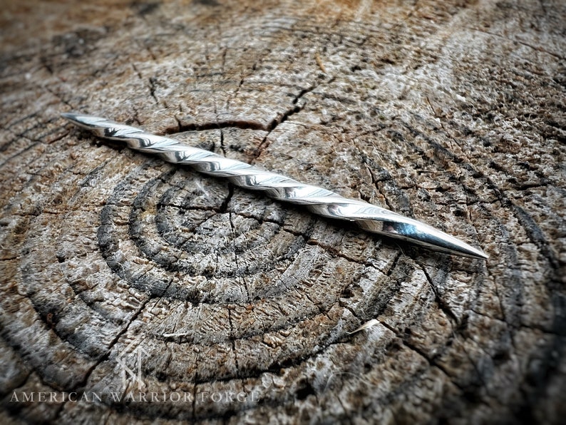 Op de afbeelding: Een zilveren gedraaide metalen punt met een scherpe punt, liggend op een houten oppervlak.