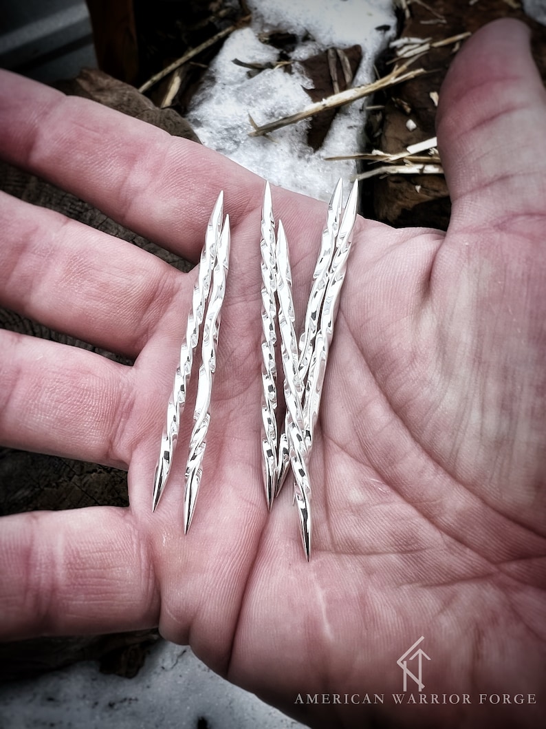 Op de afbeelding: Een set van zes zilveren, gedraaide, puntige metalen staven, vastgehouden in een hand. De staven zijn ongeveer 10 cm lang.